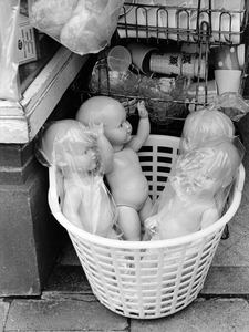 361143 Afbeelding van poppen in een plastic mand, bij een onbekende winkel.
